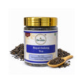 Deshla Royal Oolong Tea jar with gold lid, wooden scoop, and tea leaves on a white background