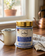 Deshla Blue Butterfly Pea Herbal Infusion jar on a wooden table with a cup and towel in the background.