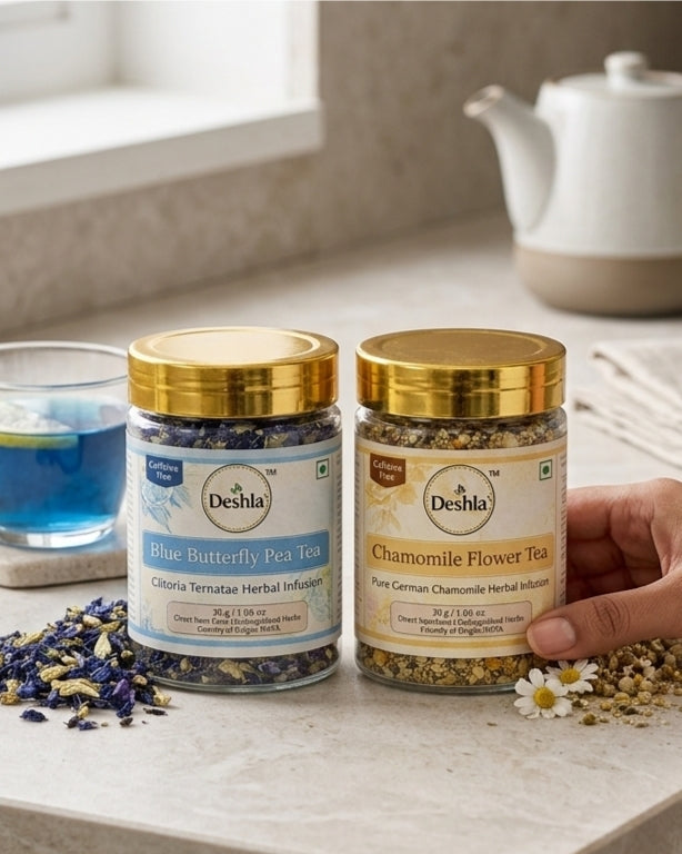 Two jars of Deshla tea on a table with a hand holding one jar, surrounded by tea leaves and a teapot.