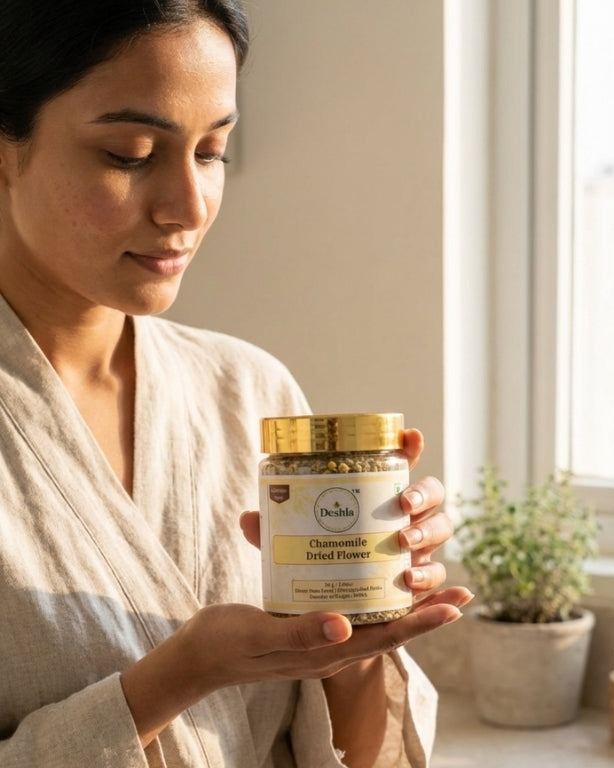 Woman holding a jar of chamomile sifted flower in a softly lit room.