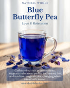 Clear mug of blue butterfly pea tea with dried flowers on a wooden surface, against a white curtain background.