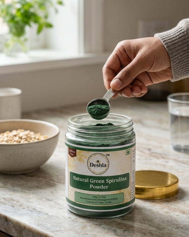Person scooping Deshla Natural Green Spirulina Powder from a jar on a kitchen counter.