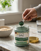 Person scooping Deshla Natural Green Spirulina Powder from a jar on a kitchen counter.