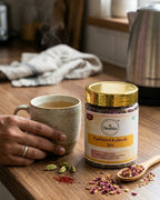 Deshla Kashmiri Kahwah tea jar on a wooden table with a cup of tea and spices.
