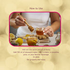 Person pouring honey into a glass of tea with lemons and spices on a blurred background.