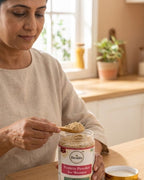 Woman scooping protein powder from a jar labeled 'Desibela' in a kitchen setting.